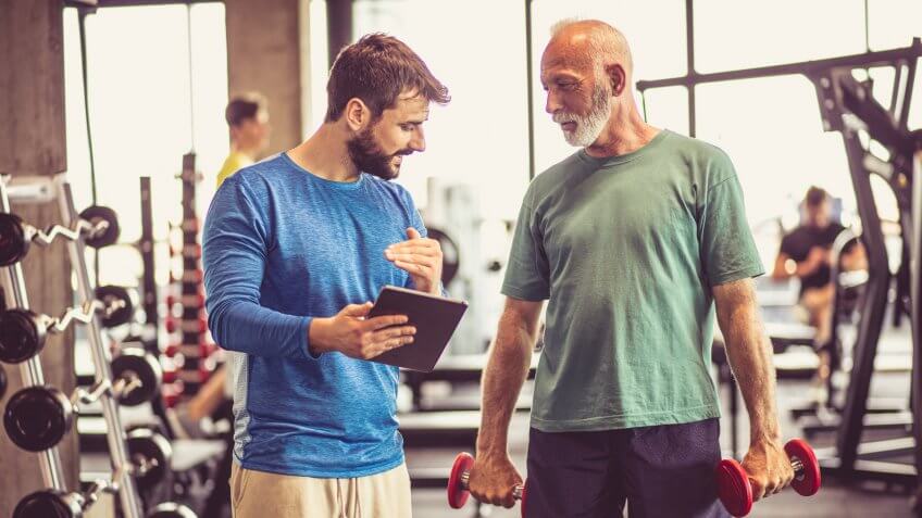 Senior man and fitness instructor talking in gym.