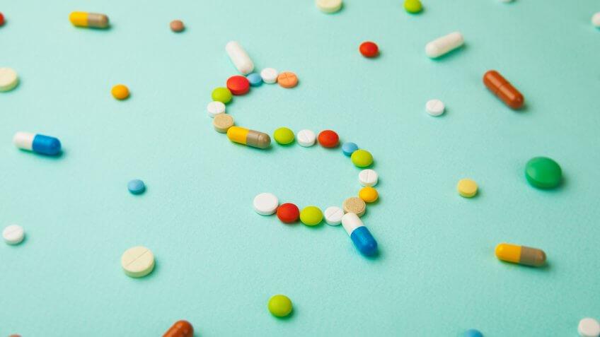Symbol of money dollar from colored pills and capsules on green background.