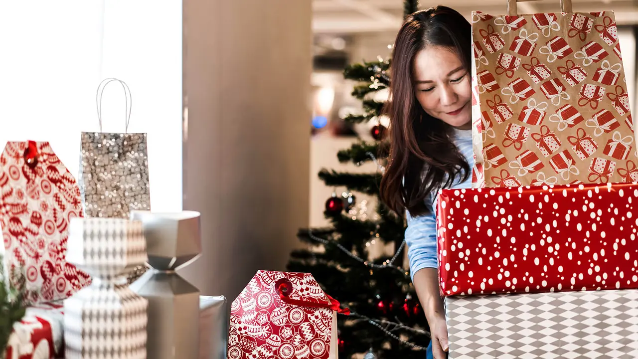 Asian woman carrying stacked of christmas gift boxes, she prepare and decorate her home for Christmas festival and night party.