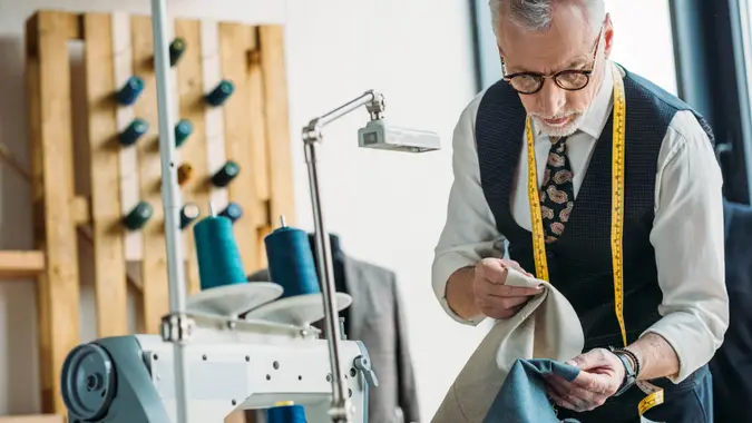 handsome tailor choosing between dark and light clothes at sewing workshop.
