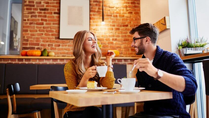 Couple of young people drinking coffee and eating cake in a stylish modern cafeteria.