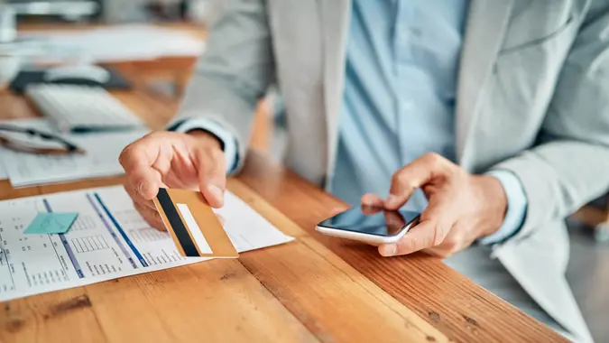 Closeup shot of an unrecognizable businessman using a cellphone while holding a credit card in an office.