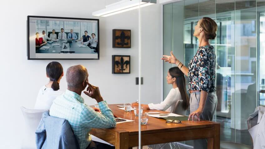 Multi-ethnic business people video conferencing at desk in board room.
