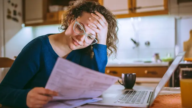 Young brunette curly female reading her bill papers, looking stressed.
