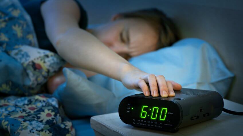 Young woman pressing snooze button on early morning digital alarm clock radio.