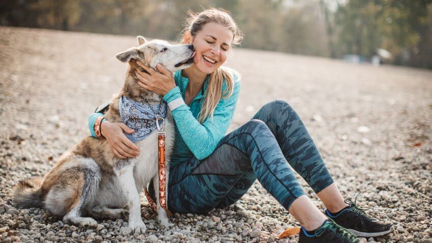 Adult woman in sports clothing spend time on beach of the lake with her dog.