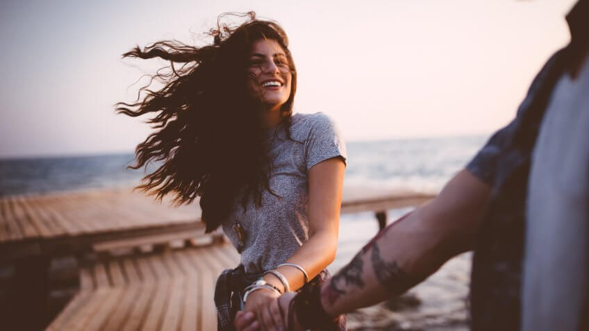 Young romantic hipster couple on summer island holidays holding hands and having fun on jetty.
