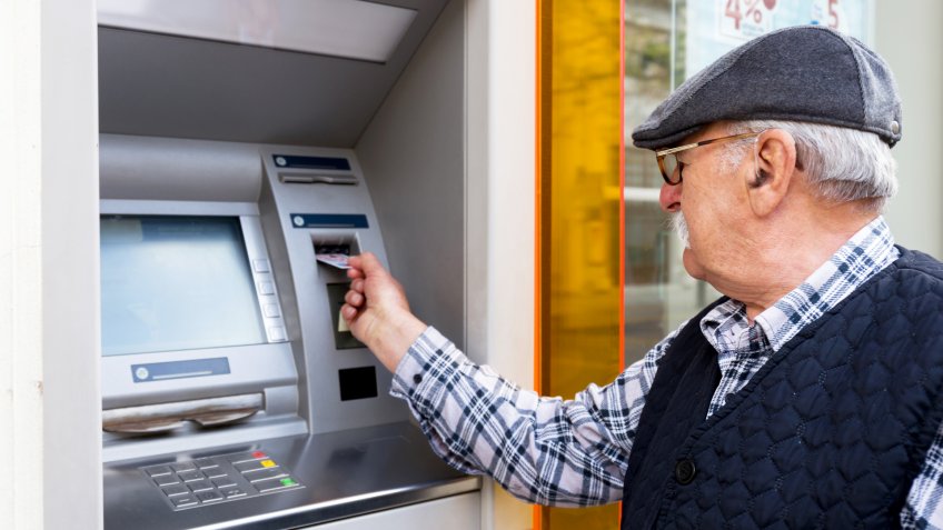 elderly man inserting credit card to ATM outdoor.