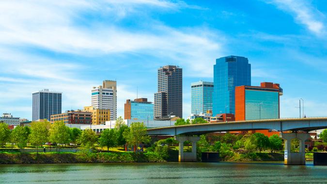 Little Rock downtown skyline with the Arkansas river in the foreground and soft wispy clouds in the background.