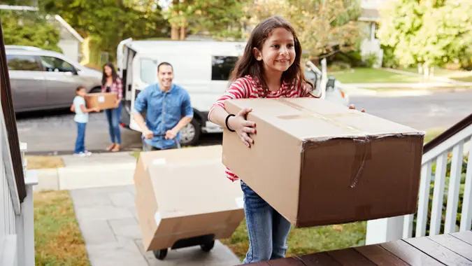 Children Helping Unload Boxes From Van On Family Moving In Day.