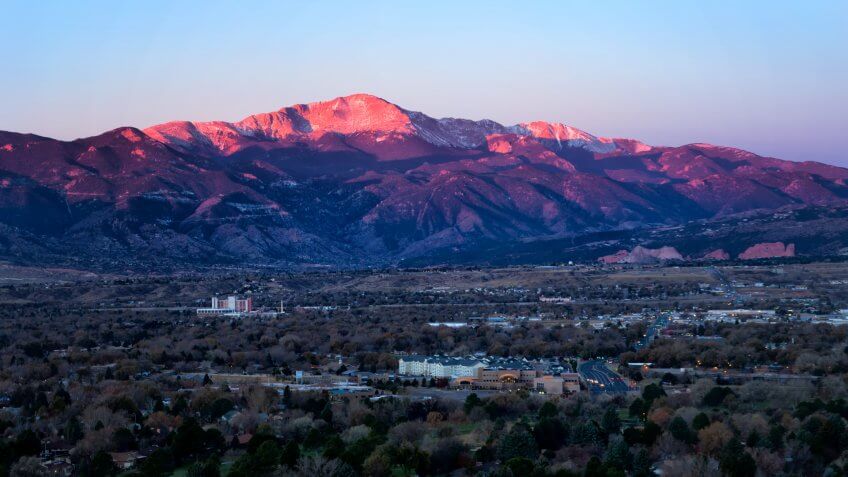 The summit of Pikes Peak glows in the morning sunrise as the streets and business office are below the mountain.