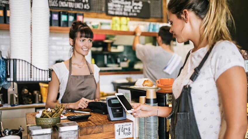 Woman paying with her mobile phone for her breakfast in a coffee Shop.
