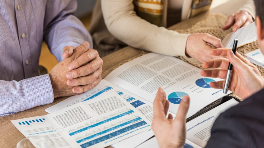 Financial advisor discussing bank details with mature couple at home.