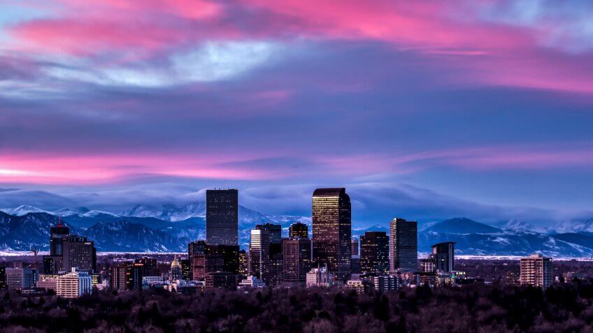 Photography of the Denver Skyline at Sunset with snowy winter peaks in distance.