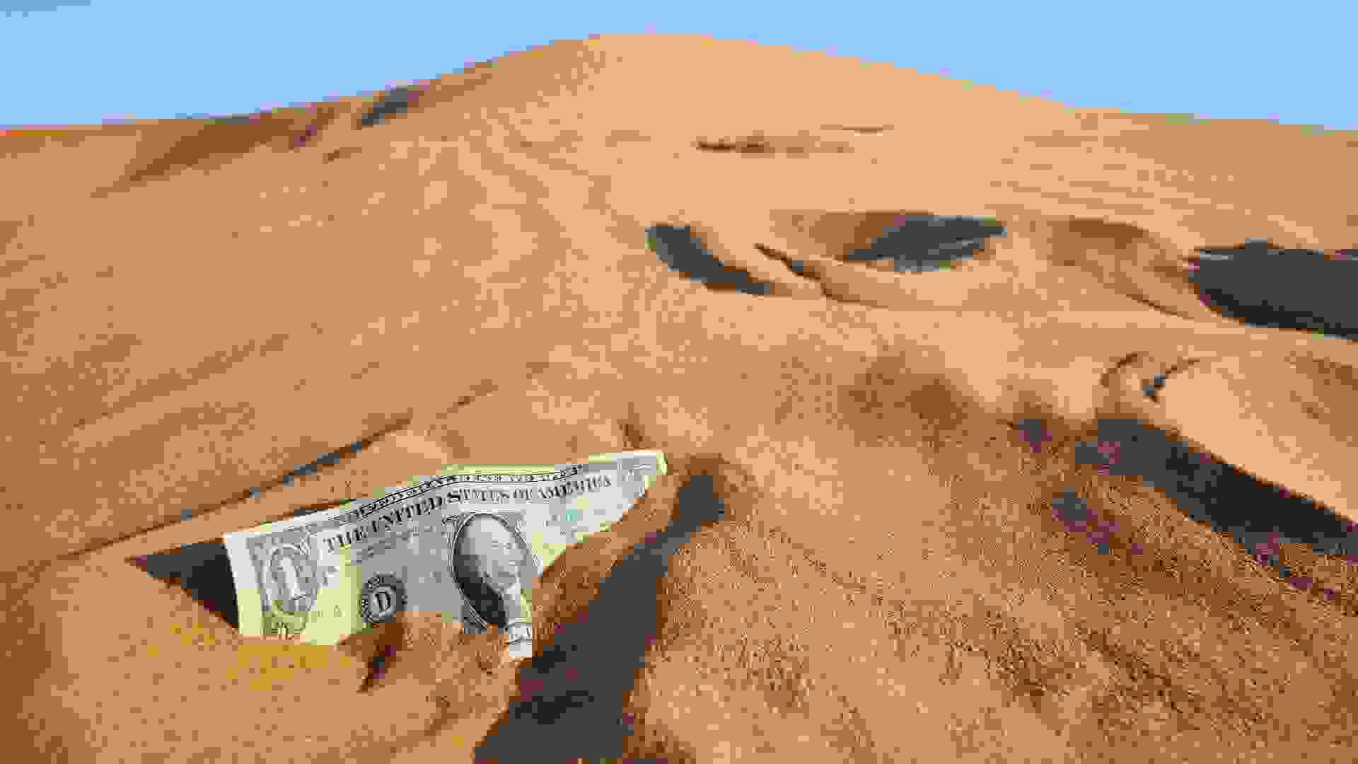 close up of dollar bill stuck in sloping sand, concept image of financial crisis and related currency turmoils.