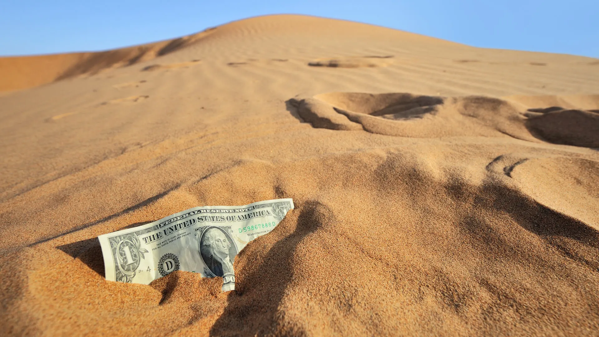 close up of dollar bill stuck in sloping sand, concept image of financial crisis and related currency turmoils.