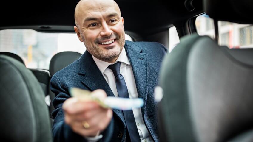 Happy passenger giving money to the driver in car.
