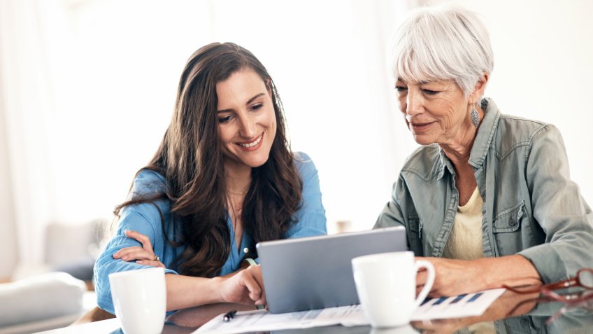 Shot of a young woman using a digital tablet with her elderly mother to help work on her home finances.