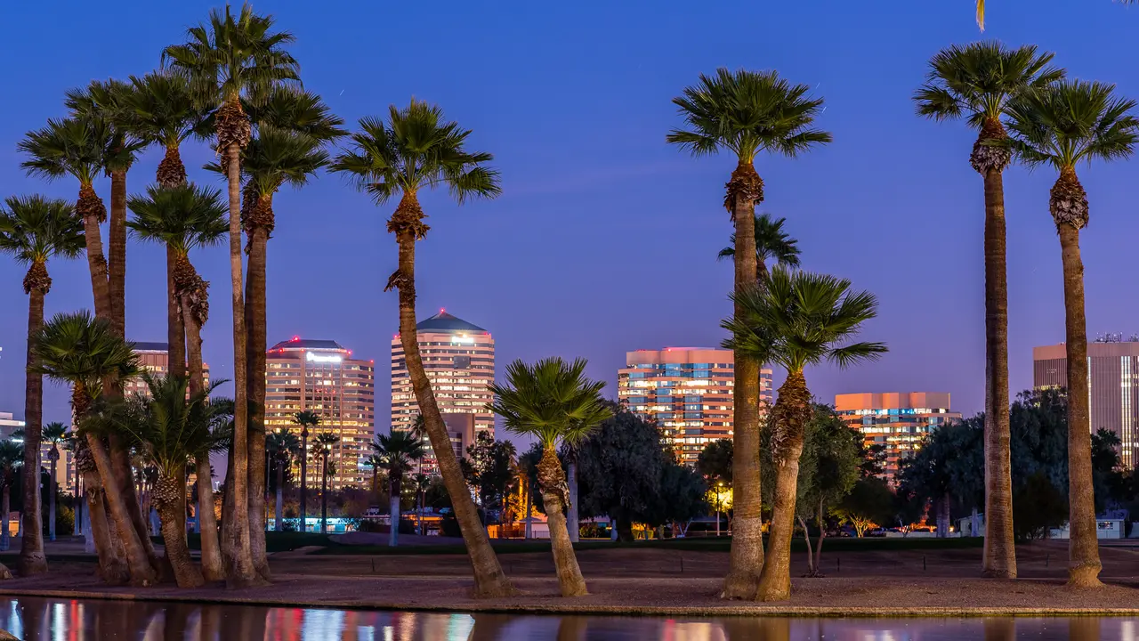 The lights of downtown Phoenix office buildings are reflected in the waters of the Encanto Park lagoon.