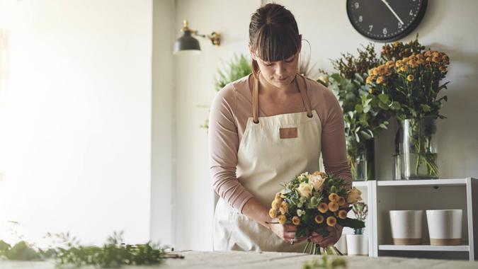 Young female florist putting together a bouquet of mixed flowers while working at a table in her flower shop.