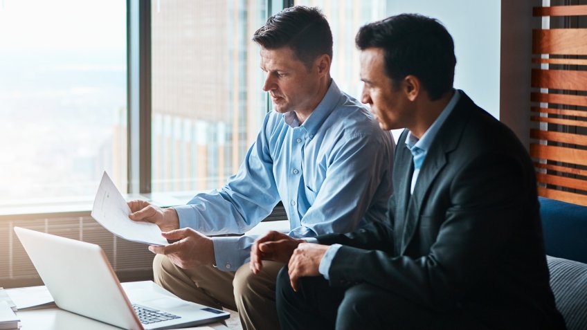 Shot of two businessmen having a discussion while sitting by a laptop.