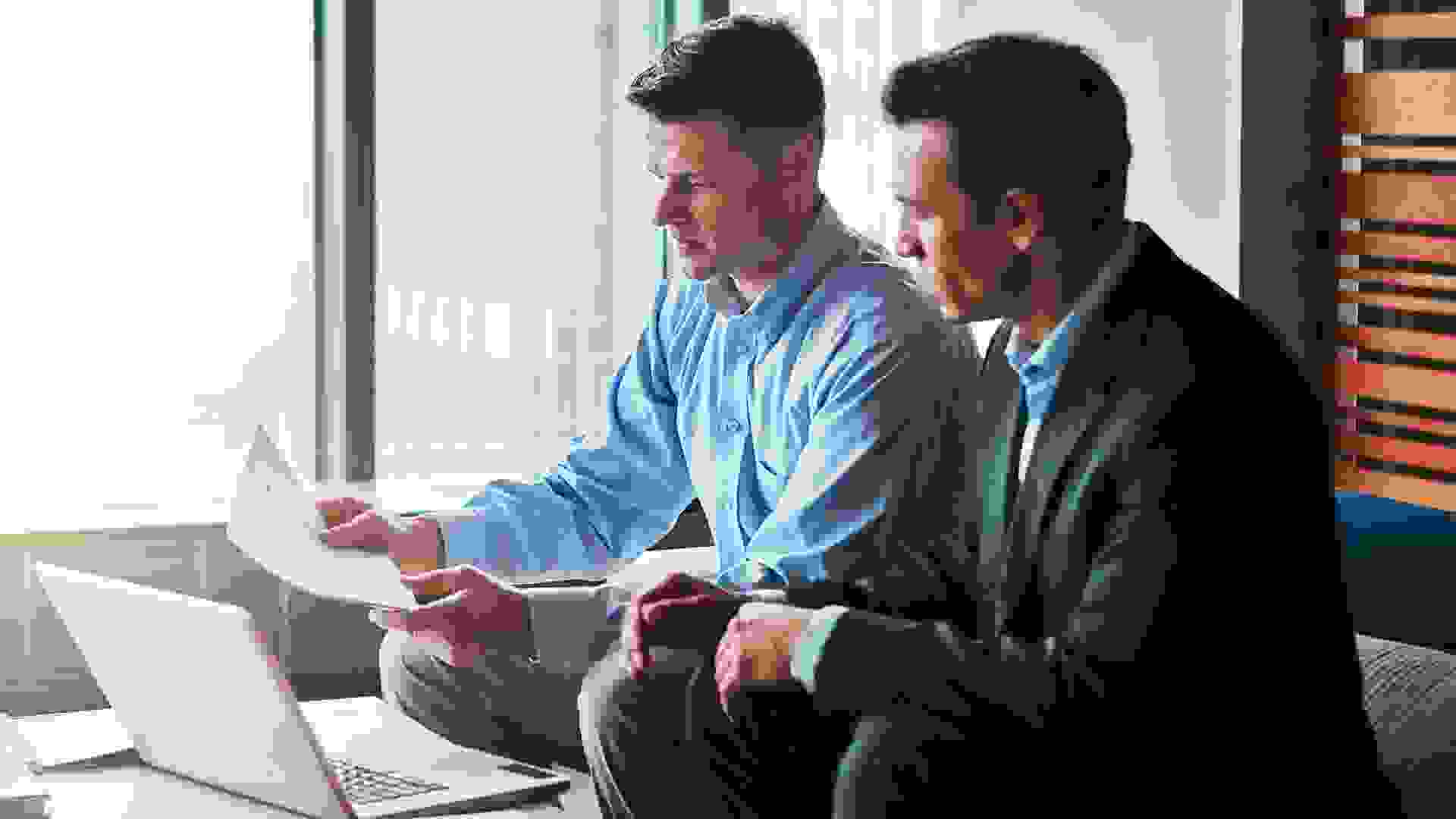 Shot of two businessmen having a discussion while sitting by a laptop.