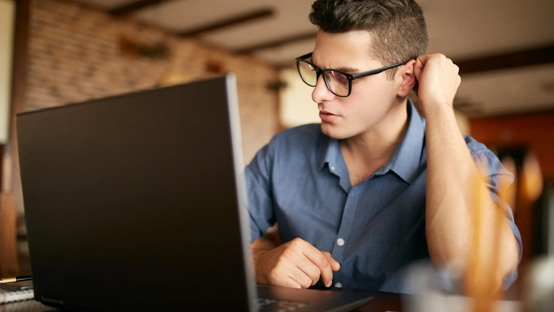 Thoughtful young caucasian businessman in glasses working on laptop computer.