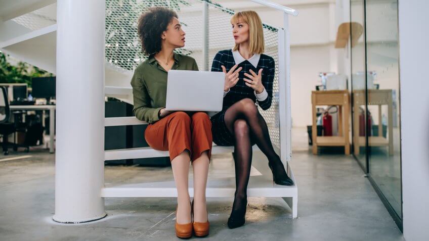 Shot of two businesswomen sitting on the stairs talking.