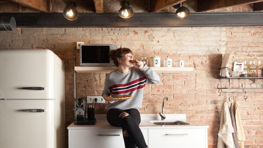Beautiful girl eating pizza in a modern kitchen.