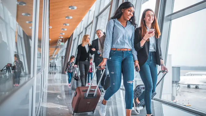 Young woman showing mobile phone to friend while business people walking in background.