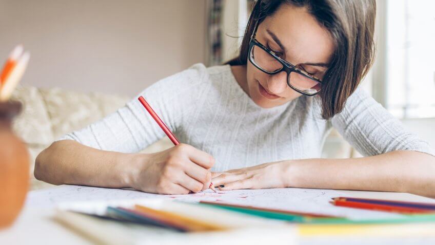Youmg woman at home coloring doodle with color pencils.