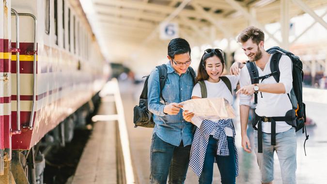 Multiethnic group of friends, backpack travelers, or college students using generic local map navigation together at train station platform.
