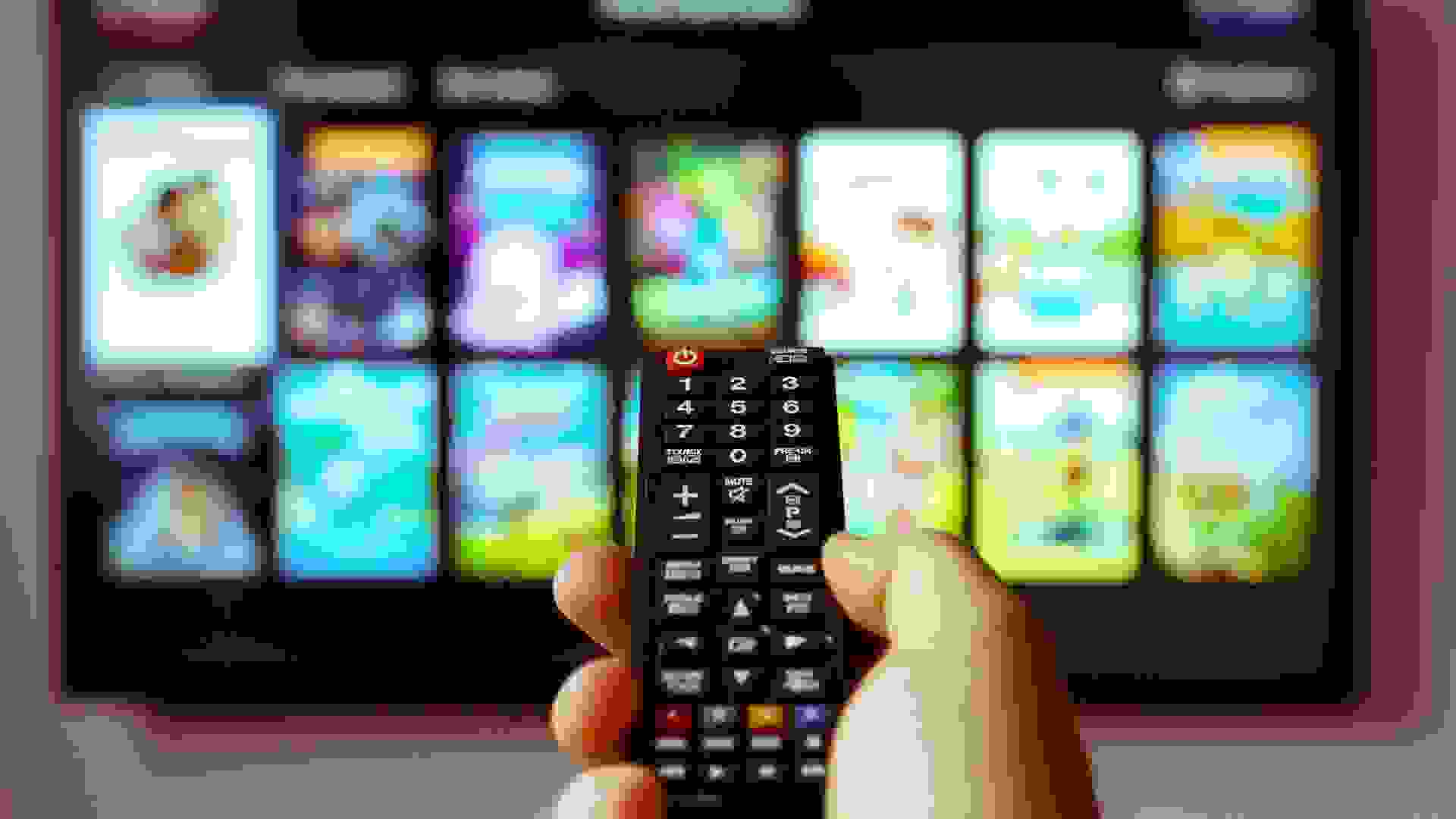 Male hand holding TV remote control.