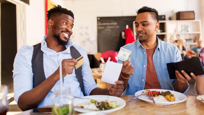 happy friends with money and credit card paying bill for food at restaurant