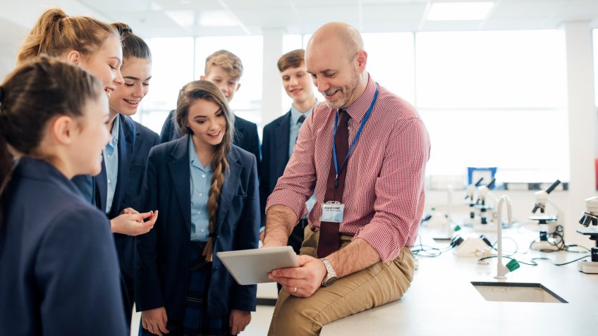 A male teacher talking to a group of students in a science room.