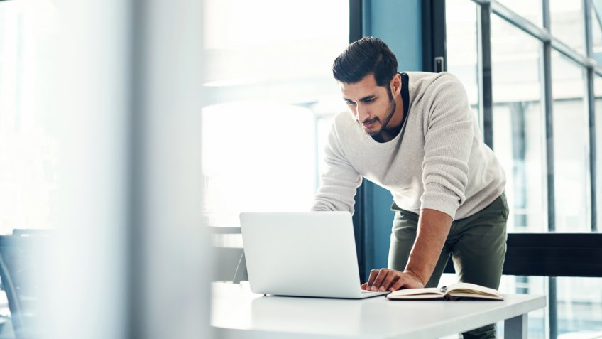 Shot of a young businessman using a laptop at his desk in a modern office.