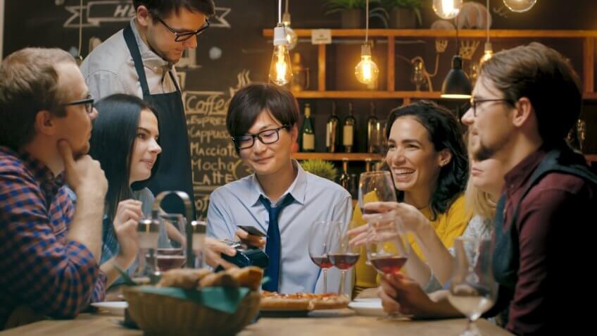 In the Bar Waiter Holds Credit Card Payment Machine and Man Pays for His Order with Contactless Credit Card.
