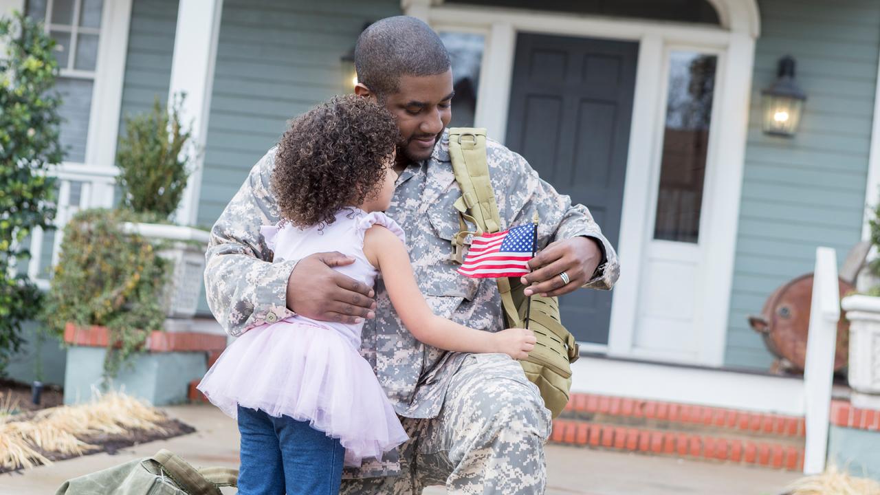 Preschool age girl hugs her soldier dad upon his return home from duty.