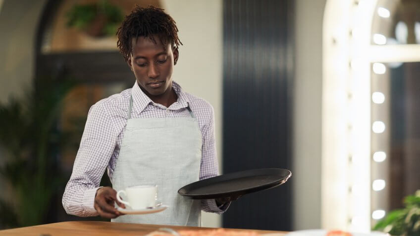 Sad waiter clearing table in restaurant.