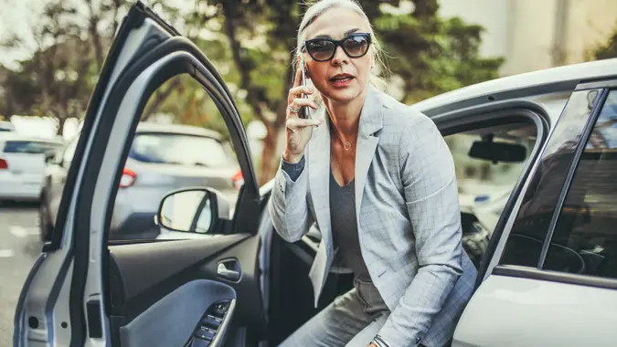 Senior businesswoman getting out of a car talking on phone.