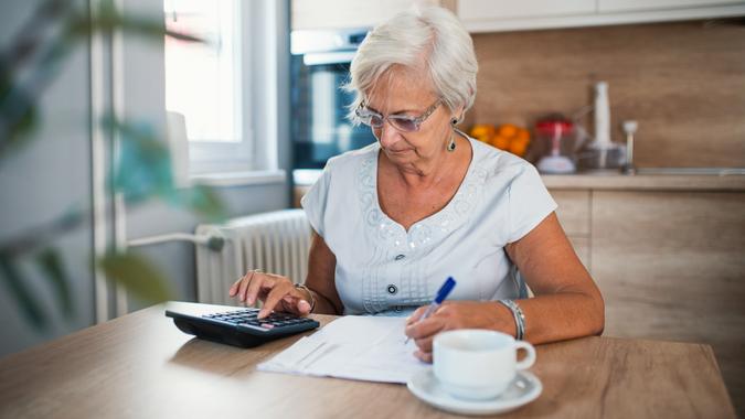 Serious elderly woman with calculator sitting at table.
