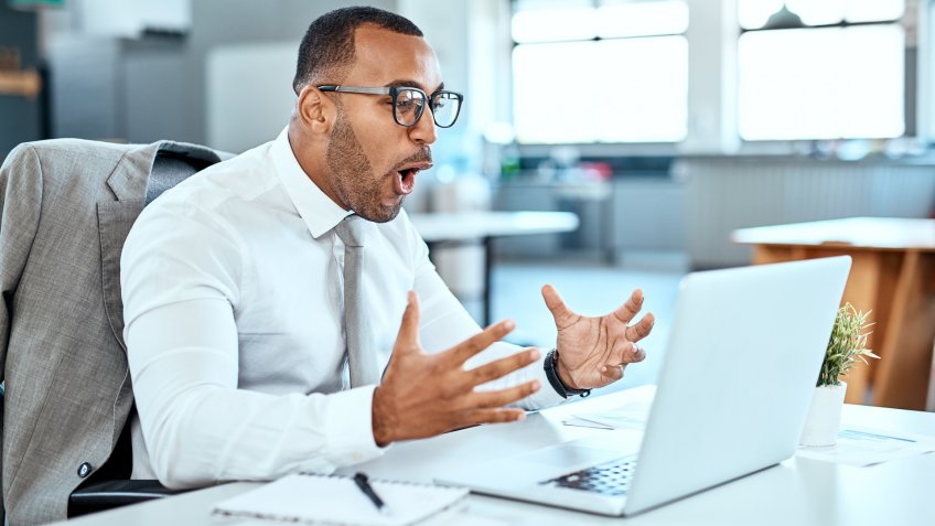 Shot of a young businessman looking surprised while working on a laptop in an office.