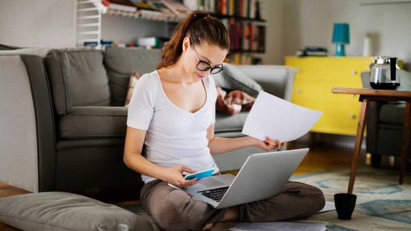 Photo of a young woman sitting on the floor and working on laptop.