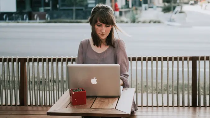 woman in gray shirt sitting on bench in front of MacBook