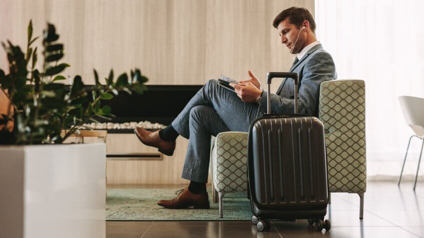 Businessman reading a magazine while waiting for his flight at airline terminal lounge.