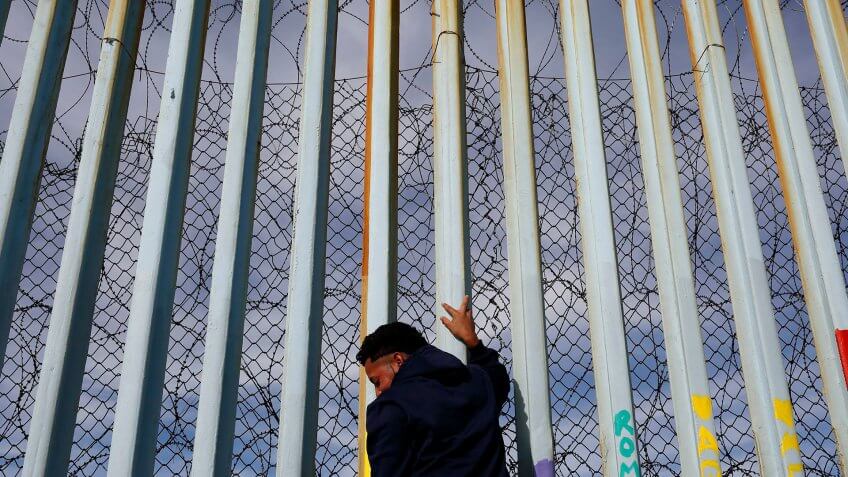A man holds on to the border wall along the beach, in Tijuana, Mexico.
