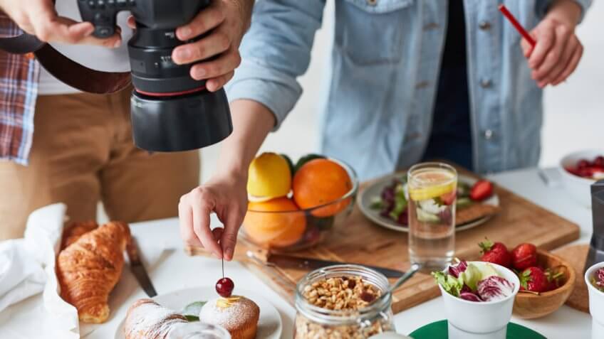 Photographer shooting food on the table while his assistant helping him