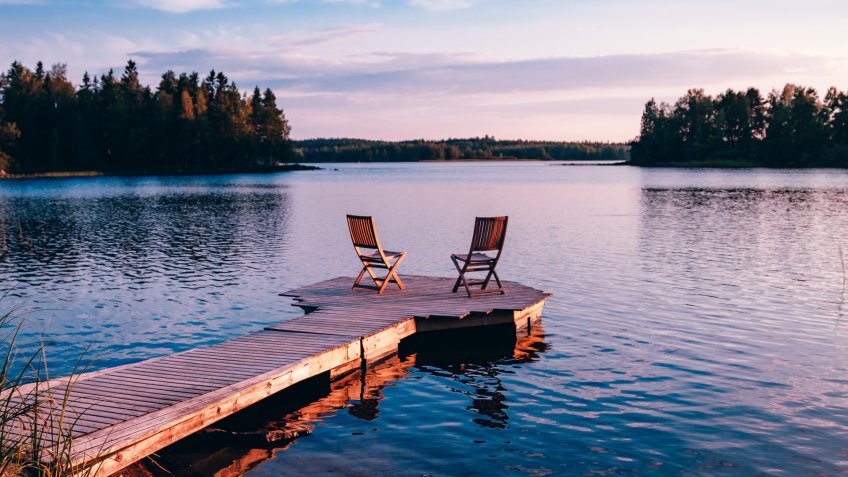 Two wooden chairs on a wood pier overlooking a lake at sunset in Finland.