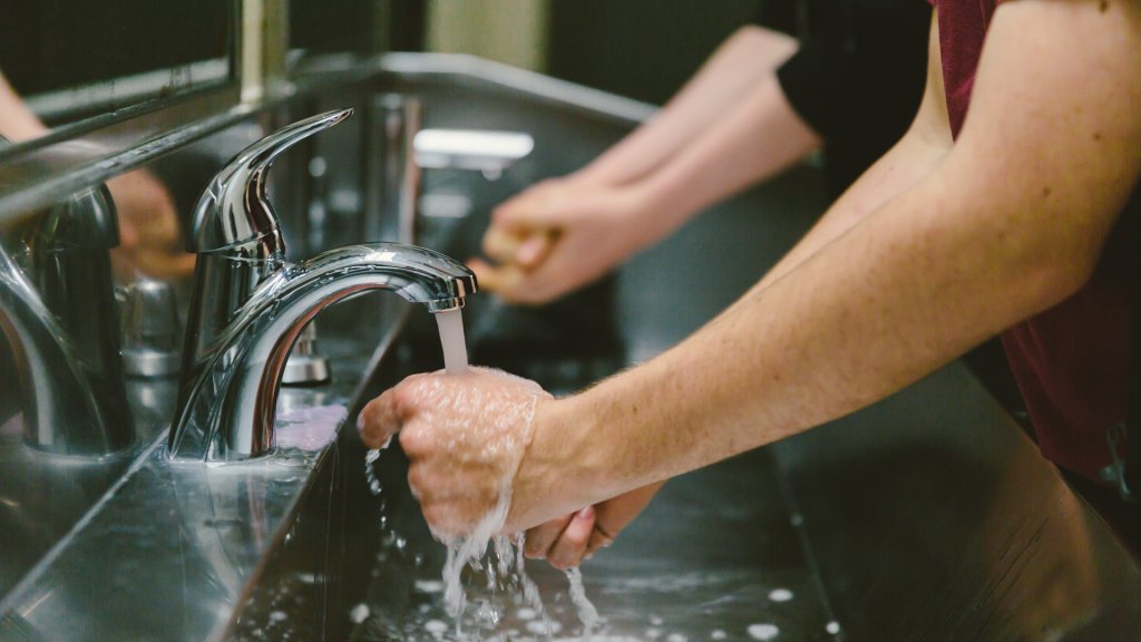 Hands washing with running water in public restroom sink.