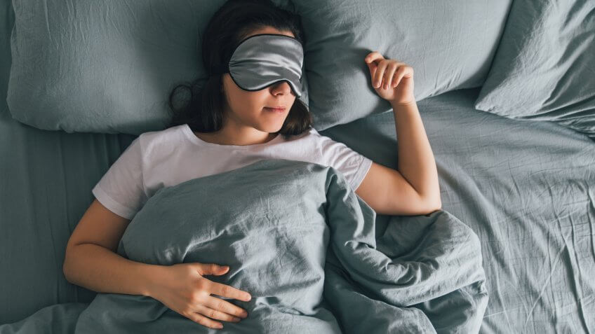 woman wearing sleeping mask in grey bed